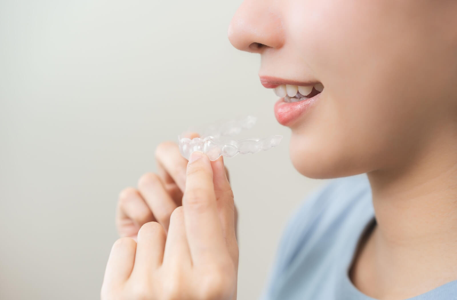 A profile view of someone is shown with them holding their Invisalign appliance.