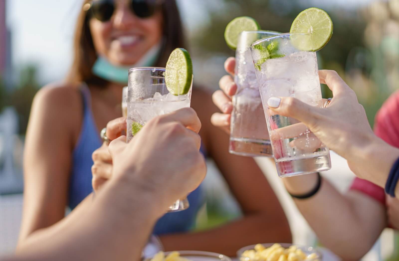A picture of a group of friends clinking their refreshing- looking glasses of seltzer water with a lime wedge, and drinking together in enjoyment.
