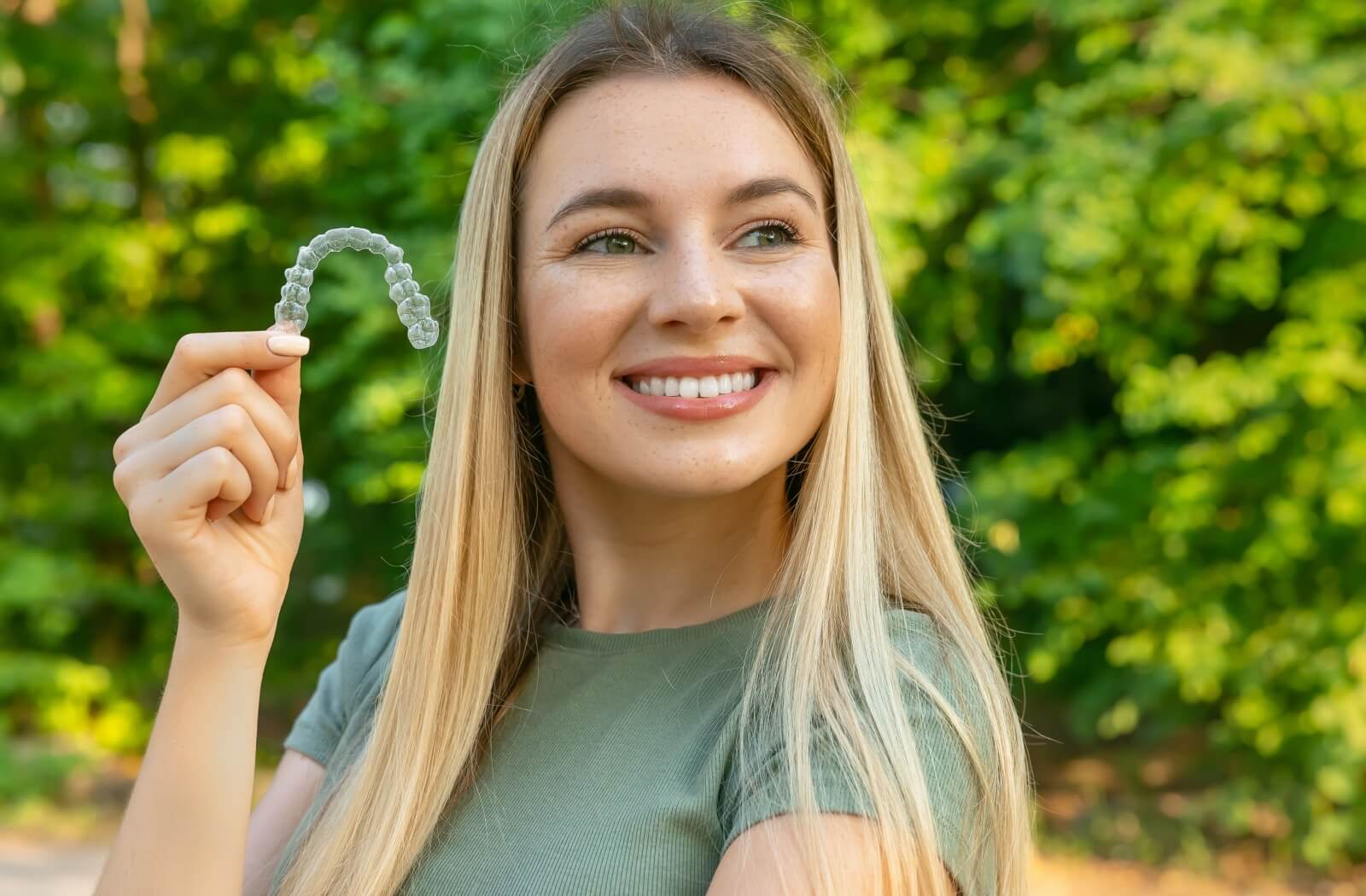 A profile view of someone is shown with them holding their Invisalign appliance.